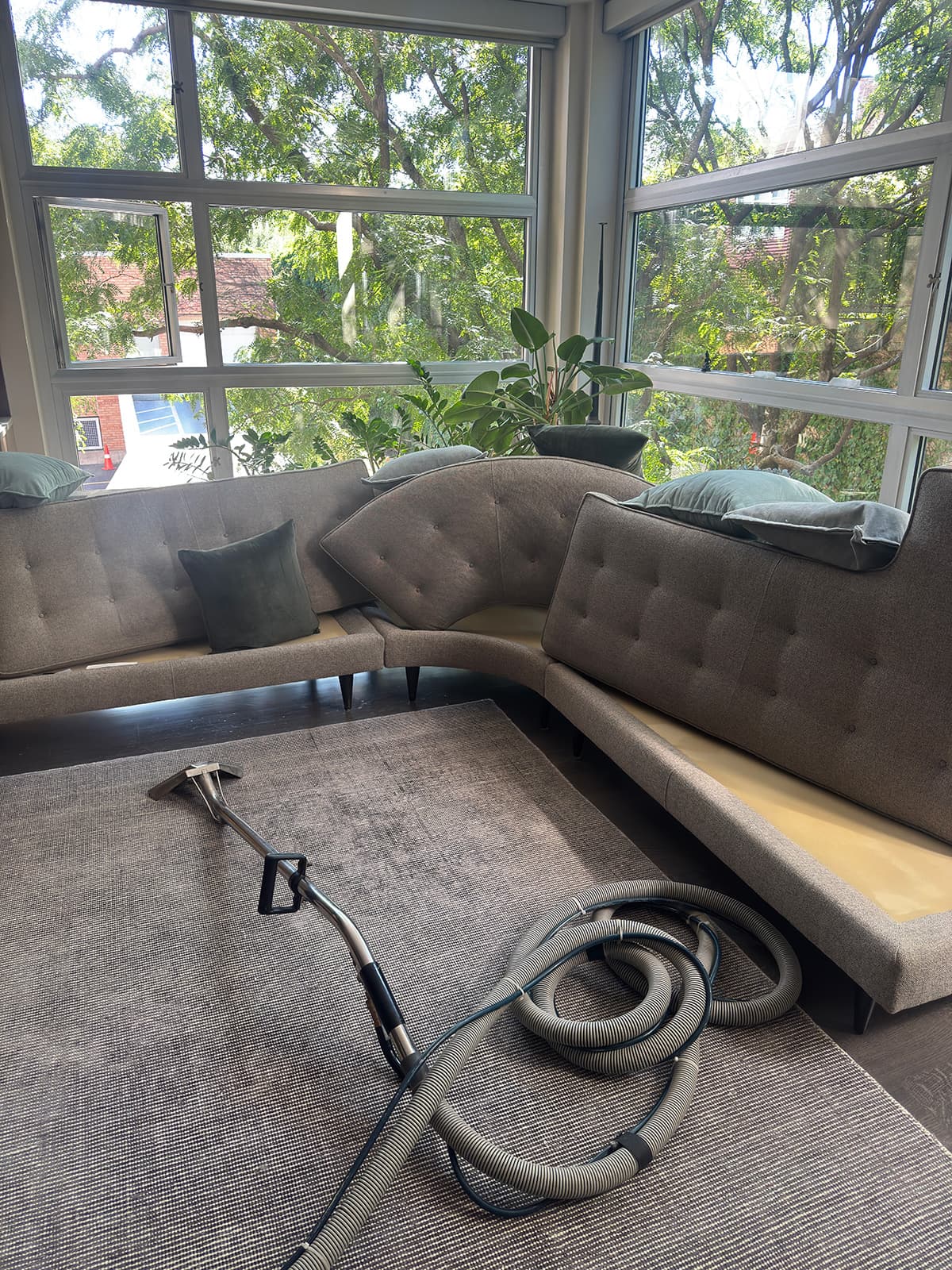 An L-shaped upholstered banquette in a window nook with the hand tool and hose laid out in front