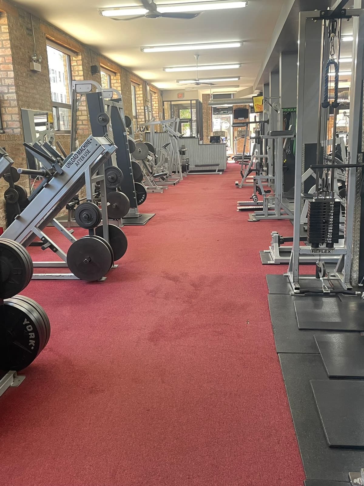 A long aisle of red gym carpet after cleaning, weight machines either side