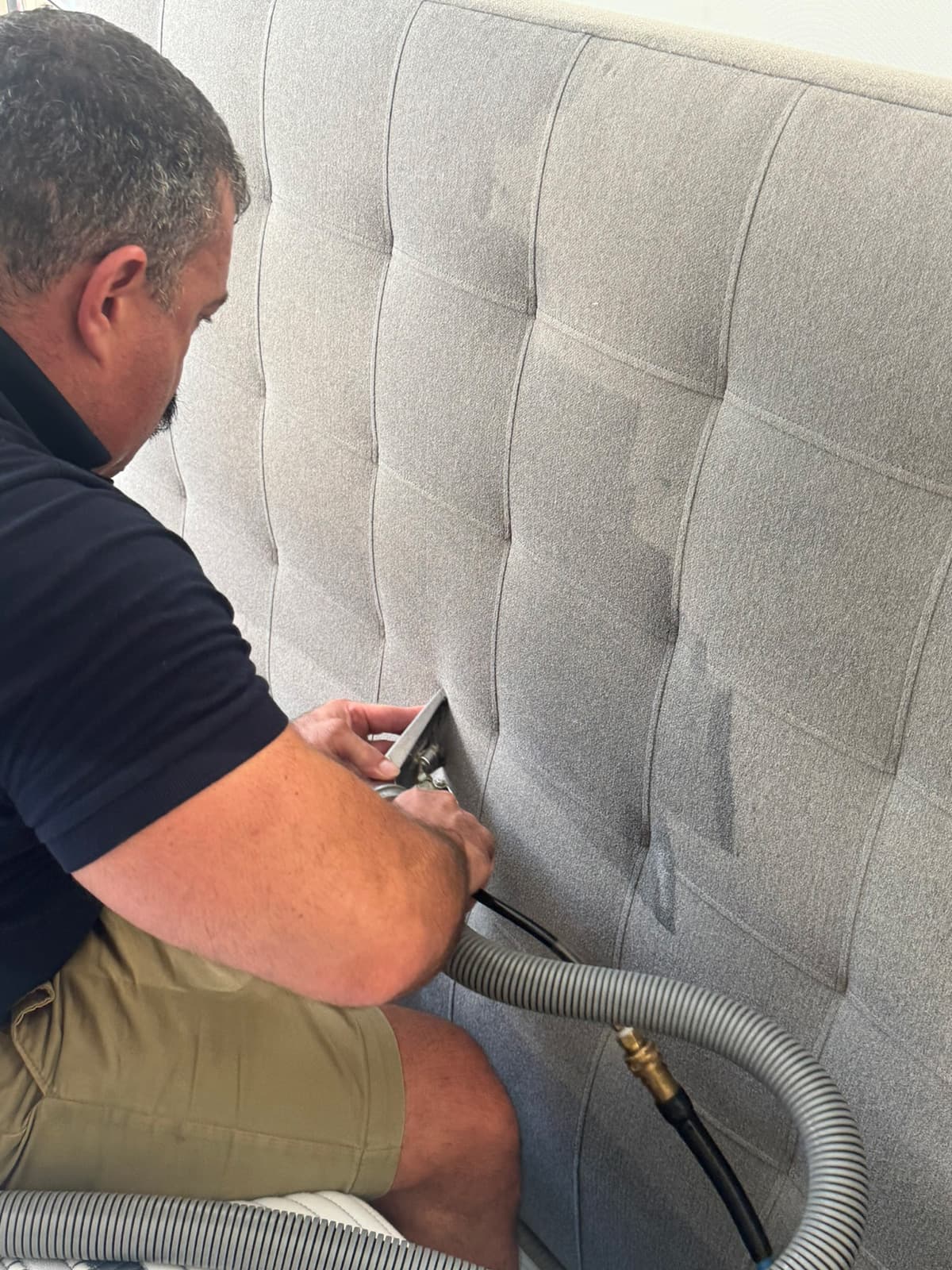 A technician working a hand tool across a tall tufted grey fabric headboard