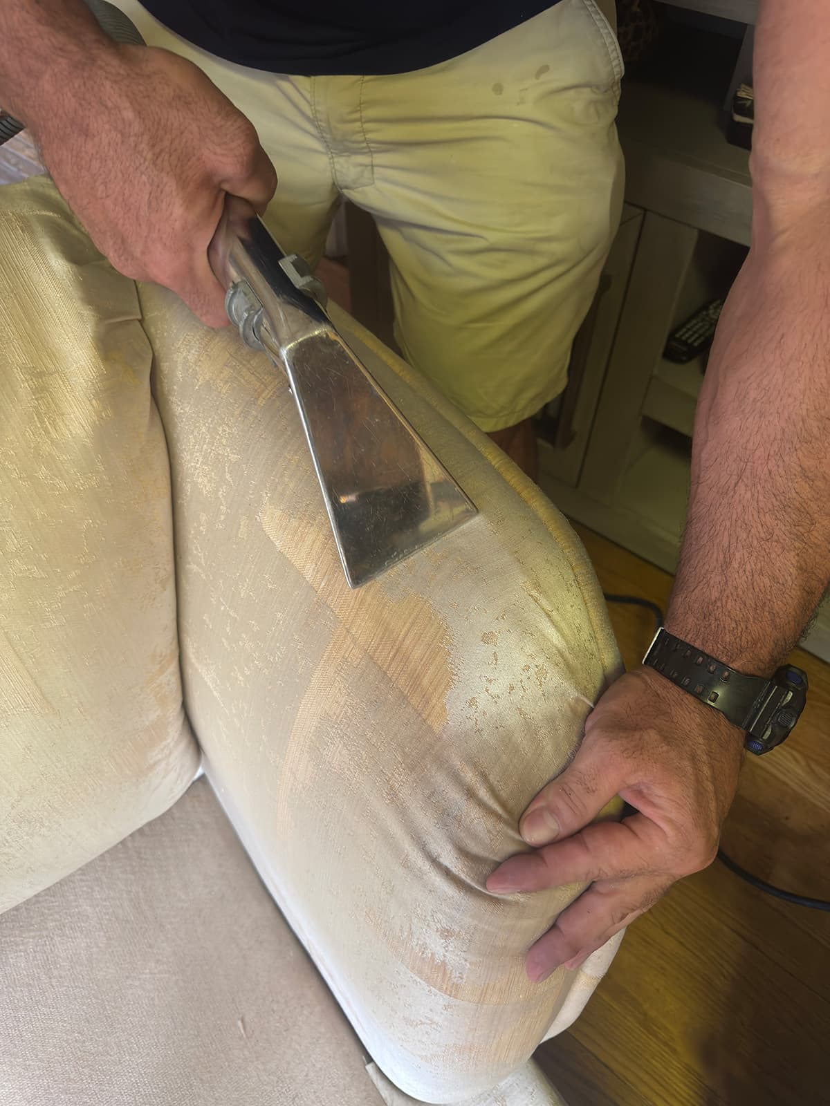 A hand tool drawn up the arm of a yellowed cream sofa, leaving a visibly cleaner stripe