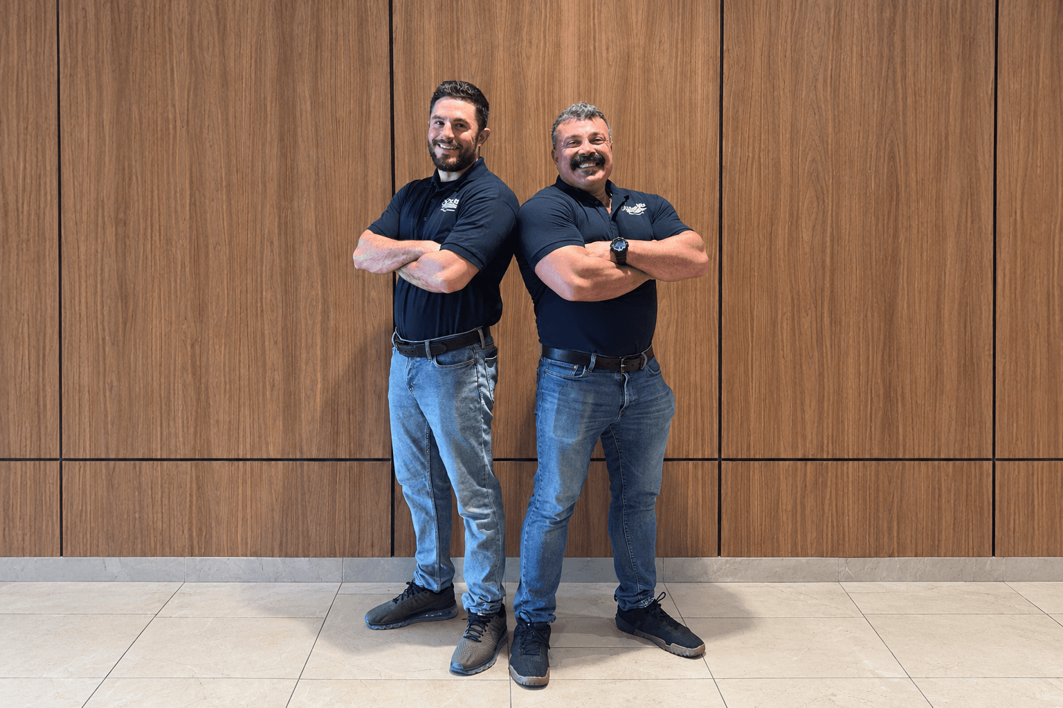 Two Clean Drs. team members in navy branded polos, standing back to back with arms crossed