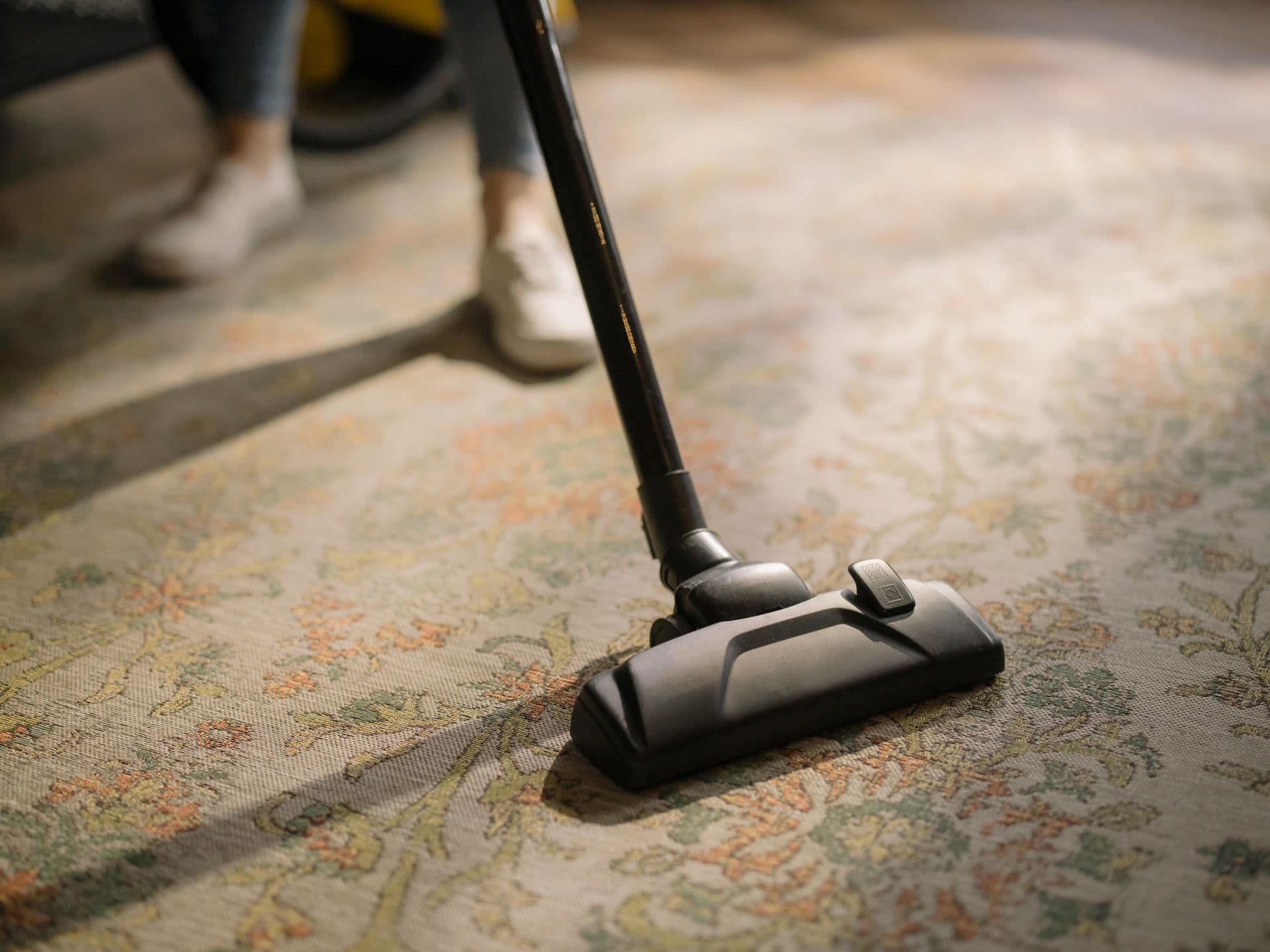 A vacuum head being pushed across a patterned carpet in a warmly lit room